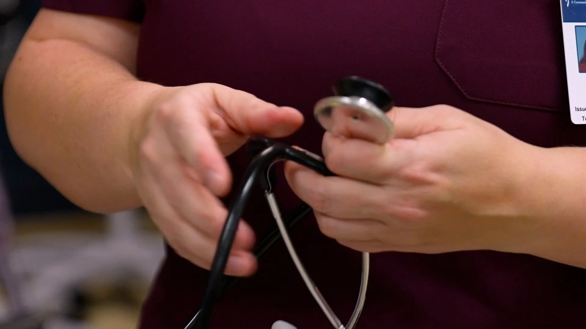 Close-up of a nursing assistant’s hands holding a stethoscope, preparing to provide hands-on patient care in a healthcare setting.
