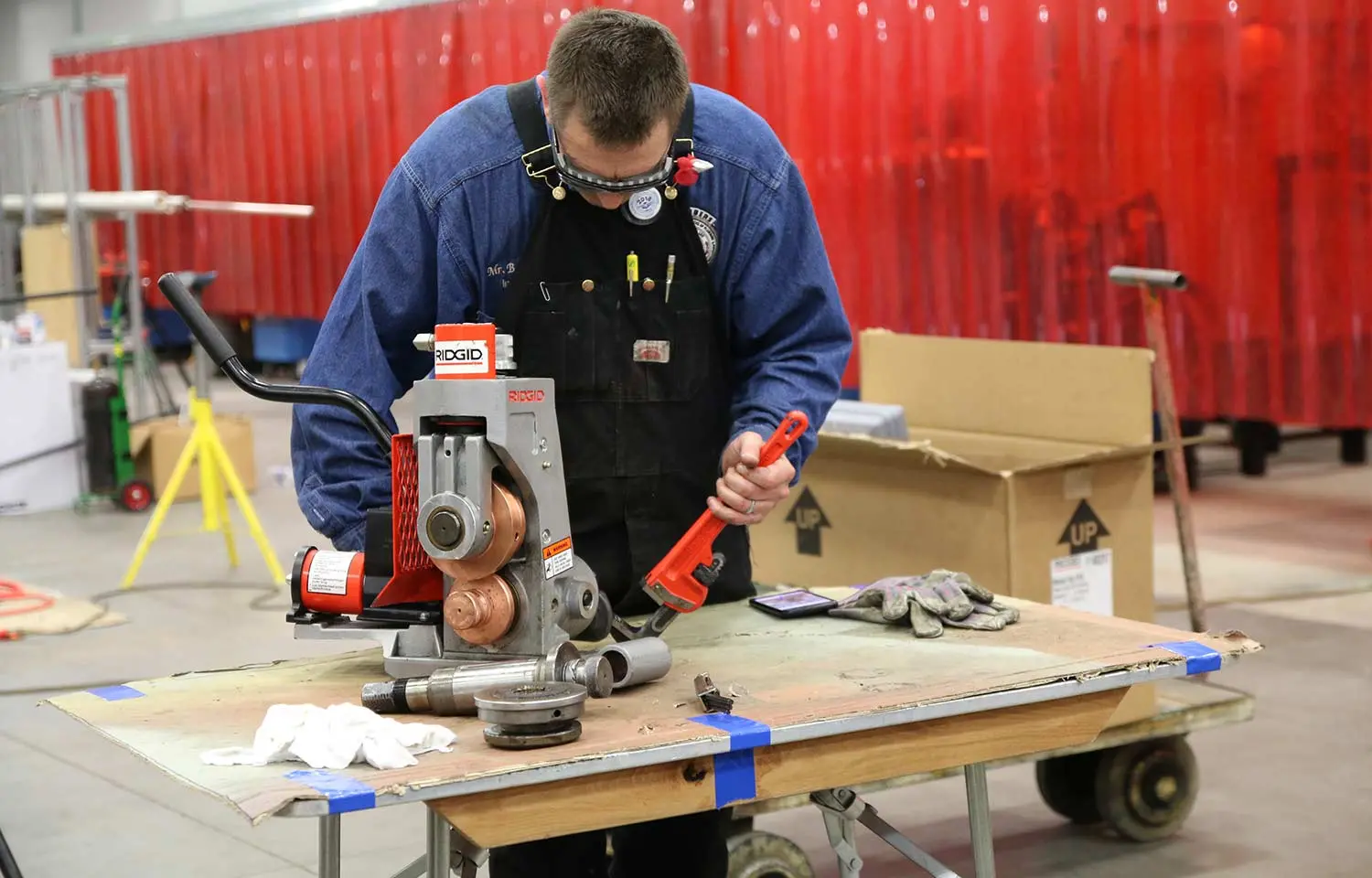student working on a pipe with tools in front of a red background