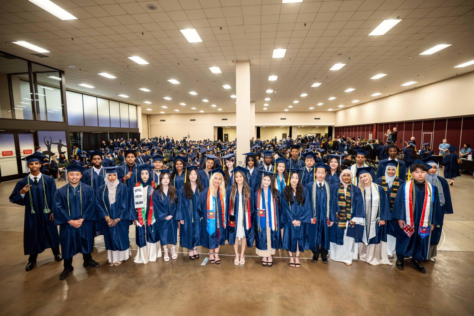 A group of graduates in blue caps and gowns standing in rows, celebrating graduation.