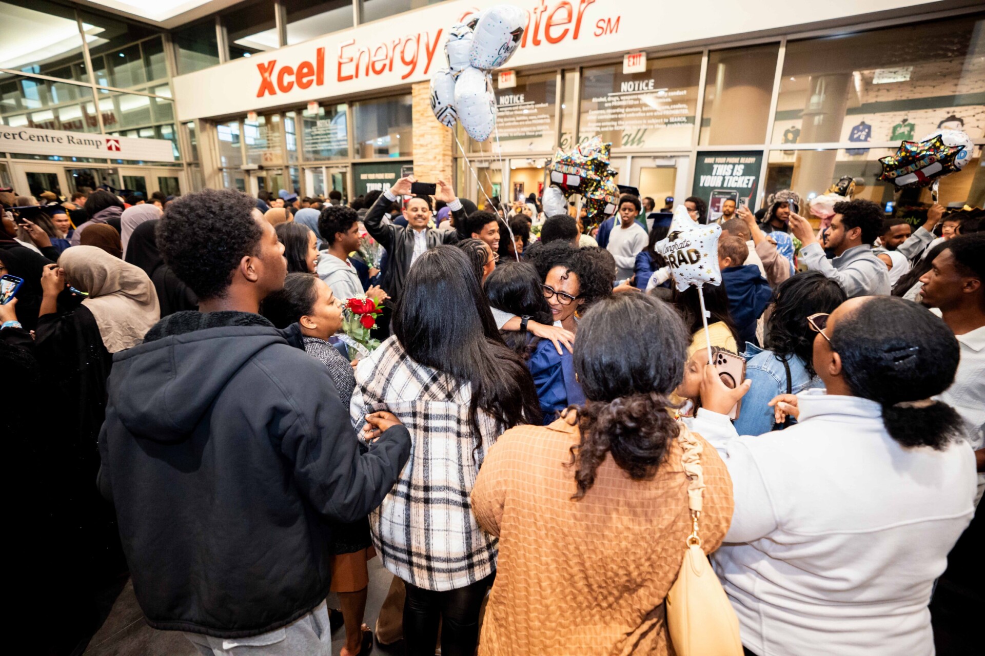 A large crowd celebrating outside the Xcel Energy Center, with balloons and flowers. People are hugging and smiling.