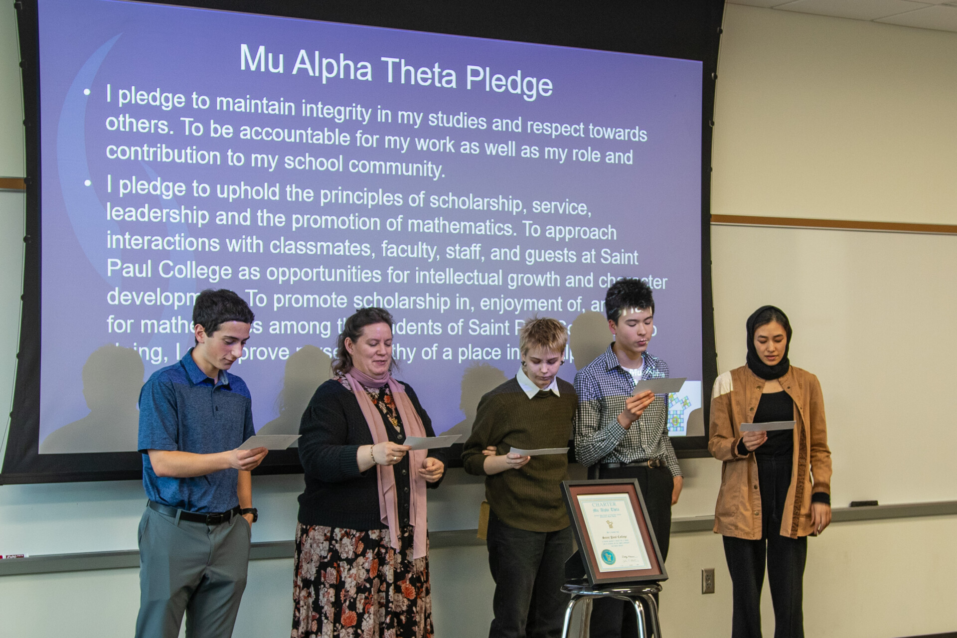 students reading in front of projection of Mu Alpha Theta pledge