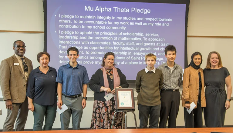 Students, faculty and Dean Onunwar in front of projection of Mu Alpha Theta pledge