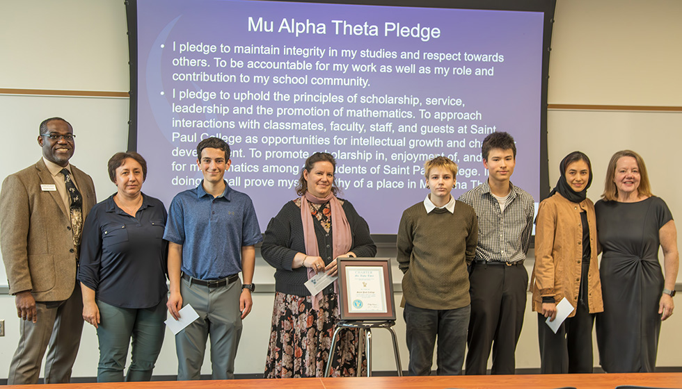 Students, faculty and Dean Onunwar in front of projection of Mu Alpha Theta pledge
