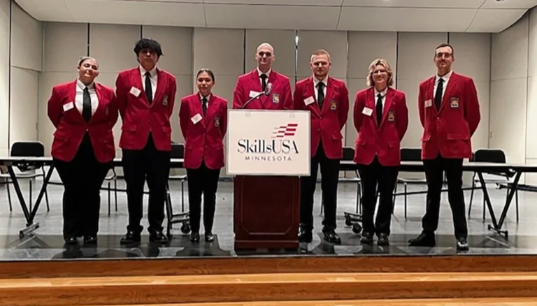 Seven students in red blazers, standing in front of a podium with SkillsUSA Minnesota logo.