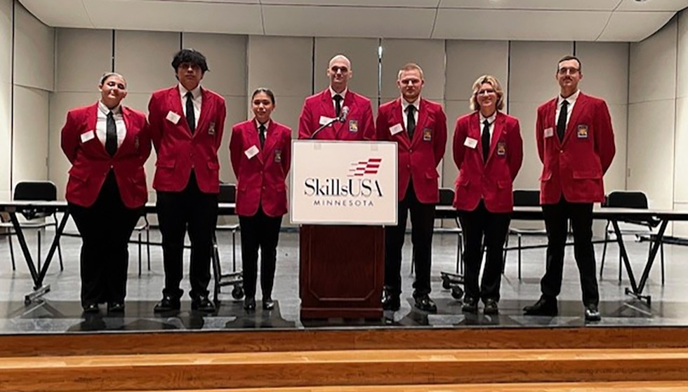 Seven students in red blazers, standing in front of a podium with SkillsUSA Minnesota logo.