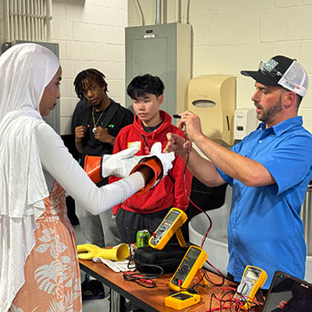 Jake Yernberg in a blue shirt teaches a student in a hijab about electrical equipment at a science table.