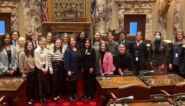 Group of young adults posing for a photo in a government chamber with ornate decor.