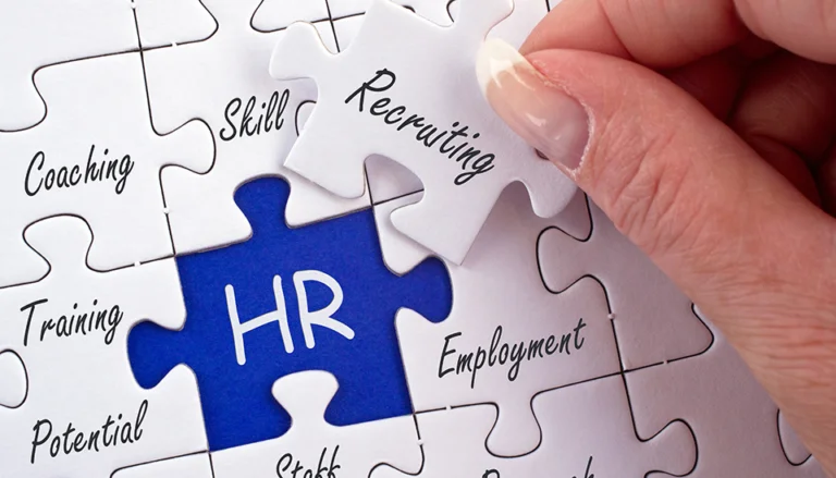 Close-up of a hand placing a puzzle piece labeled ‘Recruiting’ into a puzzle with other pieces labeled ‘Coaching,’ ‘Skill,’ ‘Training,’ ‘Employment,’ and ‘Potential,’ surrounding a central blue piece labeled ‘HR