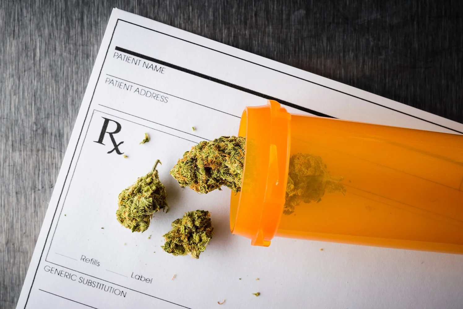 An orange prescription bottle tipped over on top of a medical form, with dried cannabis buds spilling out onto the paper.