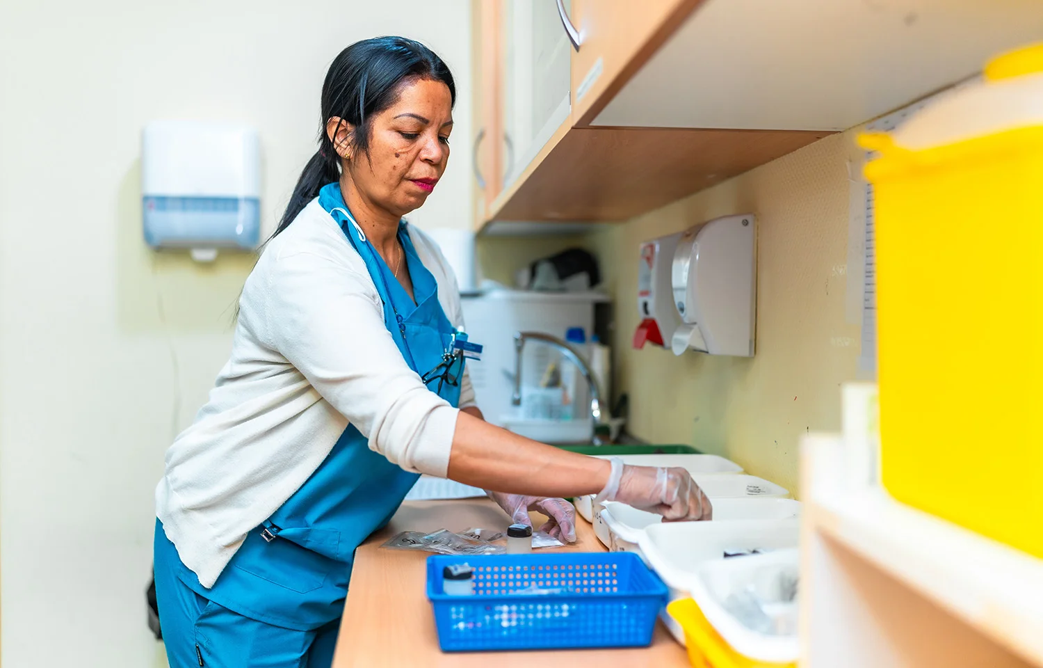 A healthcare worker wearing gloves organizing medical supplies on a counter in a clinical setting.