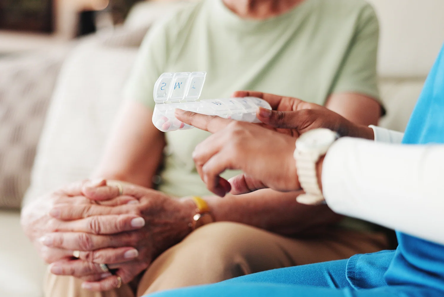 A healthcare worker showing a weekly pill organizer to an older adult, pointing to different compartments for medication management.