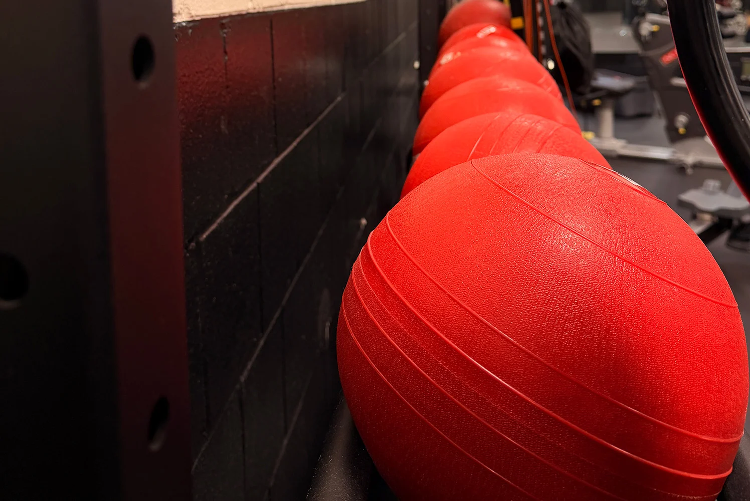Row of red exercise balls stored along a wall in a fitness training space.