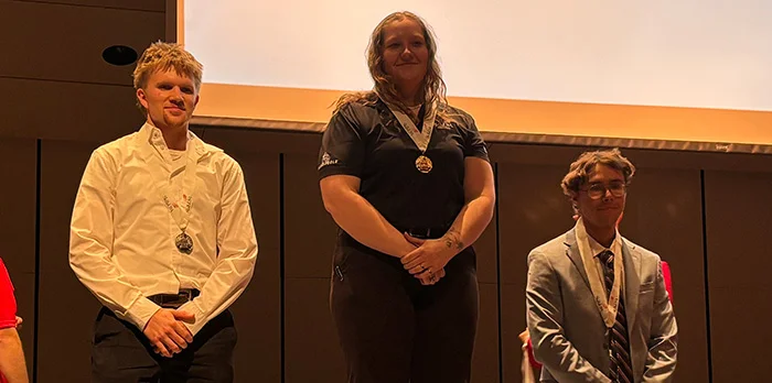 Three medal-winning competitors stand on stage at the SkillsUSA Minnesota awards ceremony, wearing medals during the podium presentation.