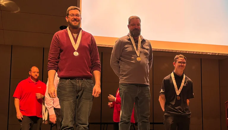 Three medal-winning competitors stand on stage at the SkillsUSA Minnesota awards ceremony, wearing medals during the podium presentation.