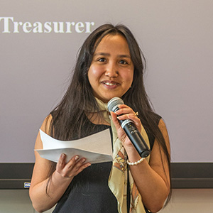 Iangotiana Adnriamantsoa holding a microphone and reading from a sheet of paper while speaking in front of a projection screen