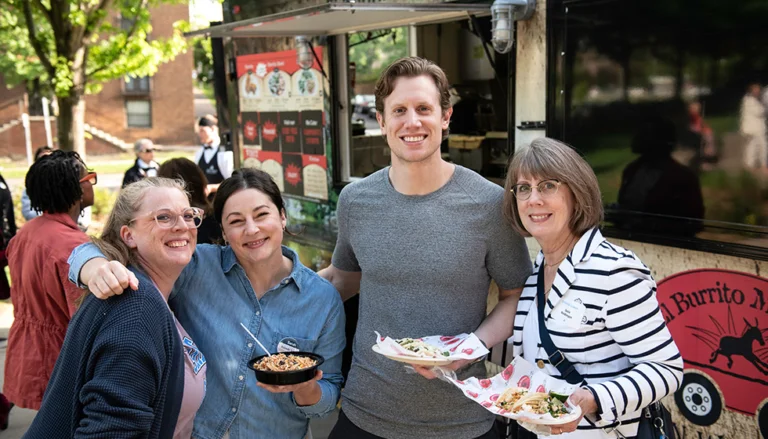 Group of people smiling at a food truck holding tacos and bowls outdoors in a park setting