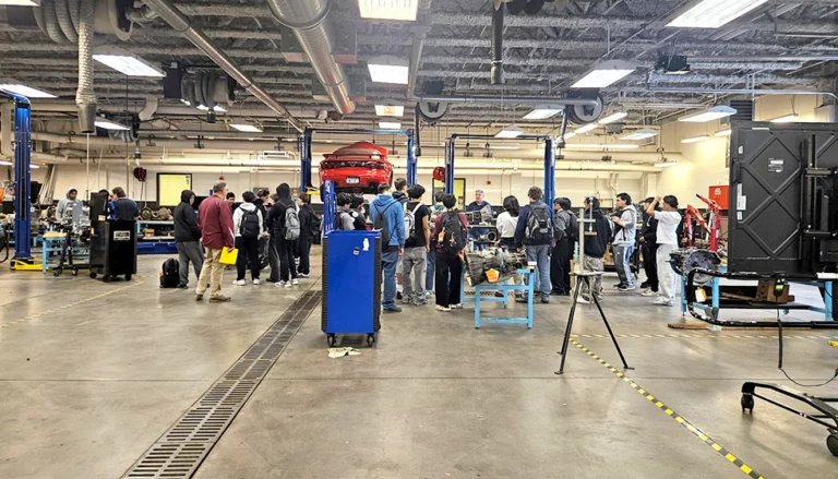 Group of high school students in an autobody shop as instructors speak to them.