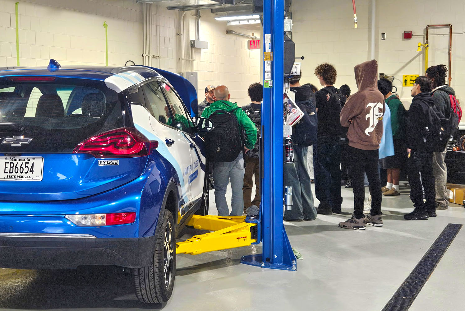 Group of high school students standing next to the hood of the Saint Paul College branded hybrid car.