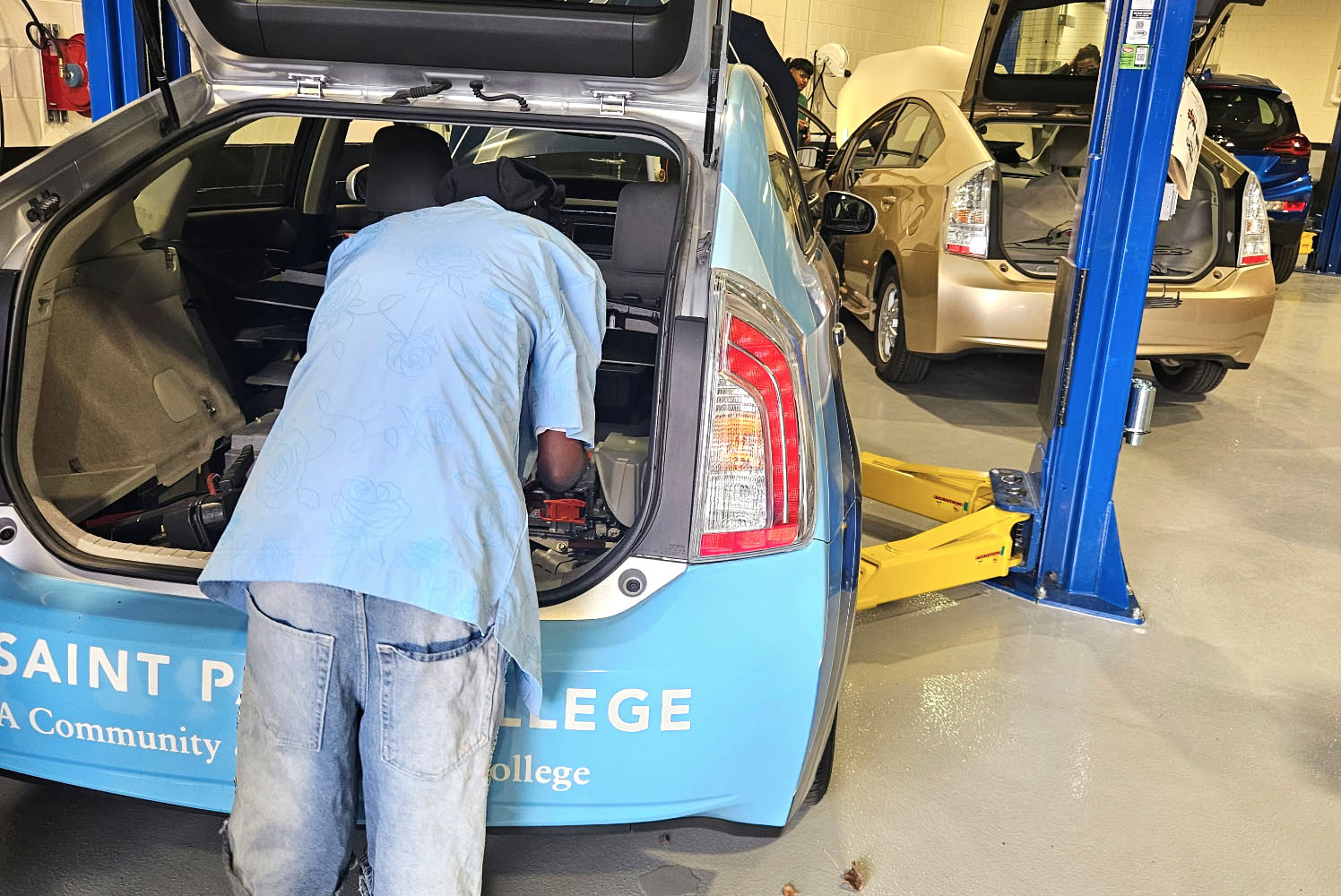 high school student working on the system of the hybrid car in the trunk of the car.