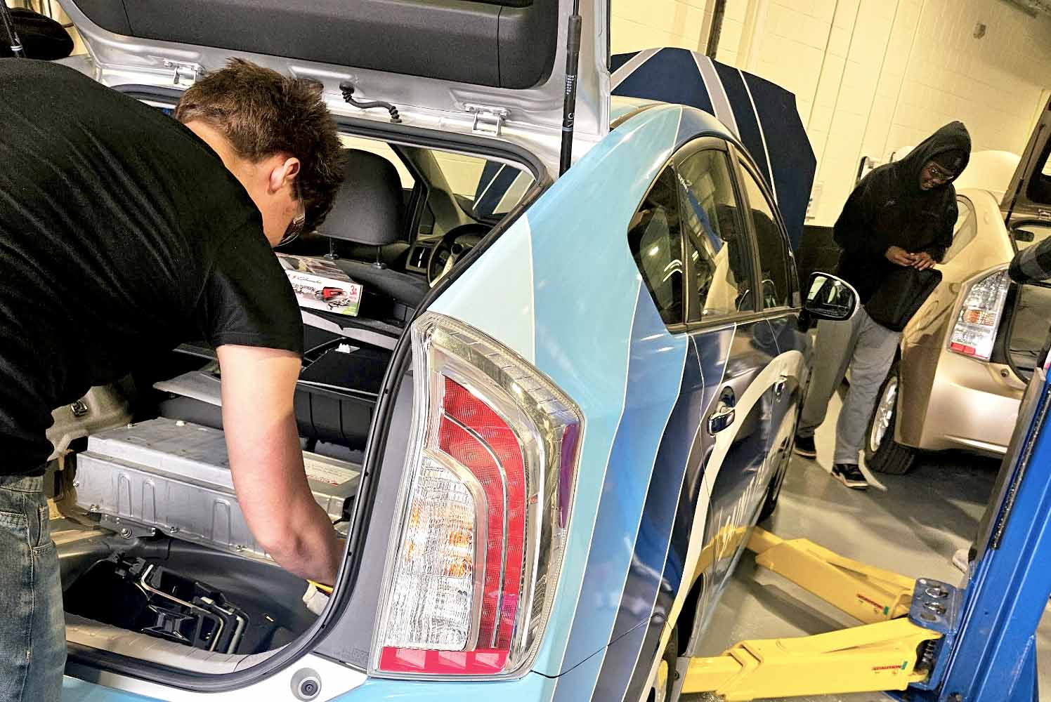 high school student working on the system of the hybrid car in the trunk of the car.