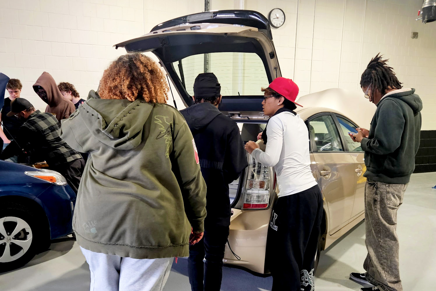 Group of high school students observing the trunk of a car in the automotive shop.