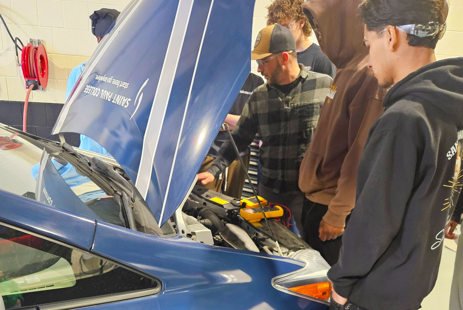 Several high school students observe under the hood of a hybrid car as the instructor is teaching.