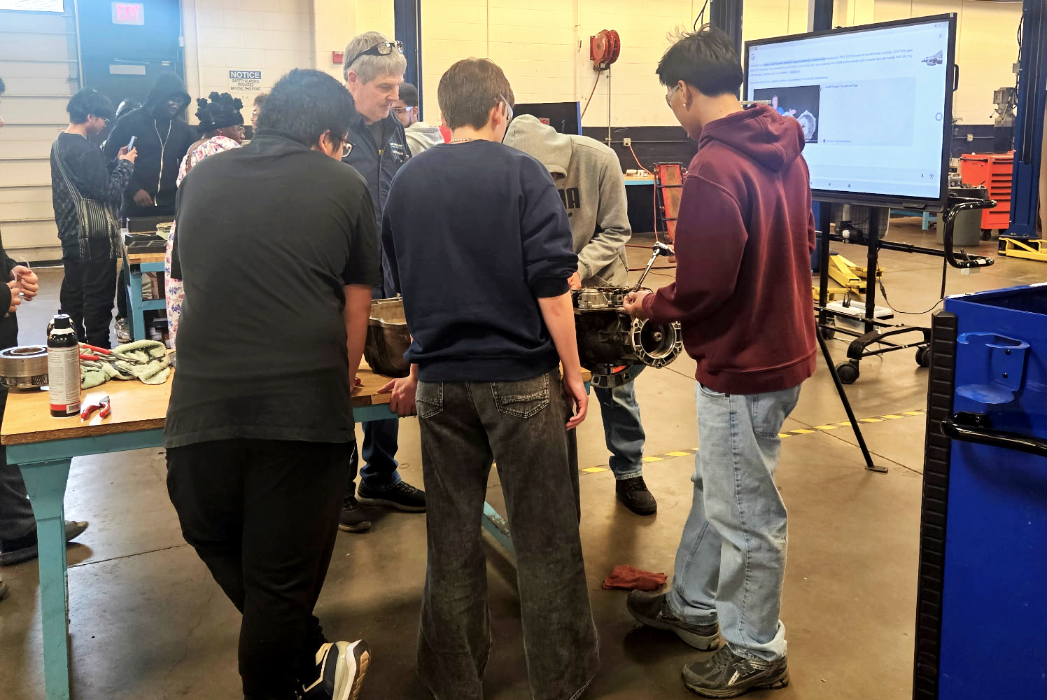 Three high school students around a table working on the transmission of a car.