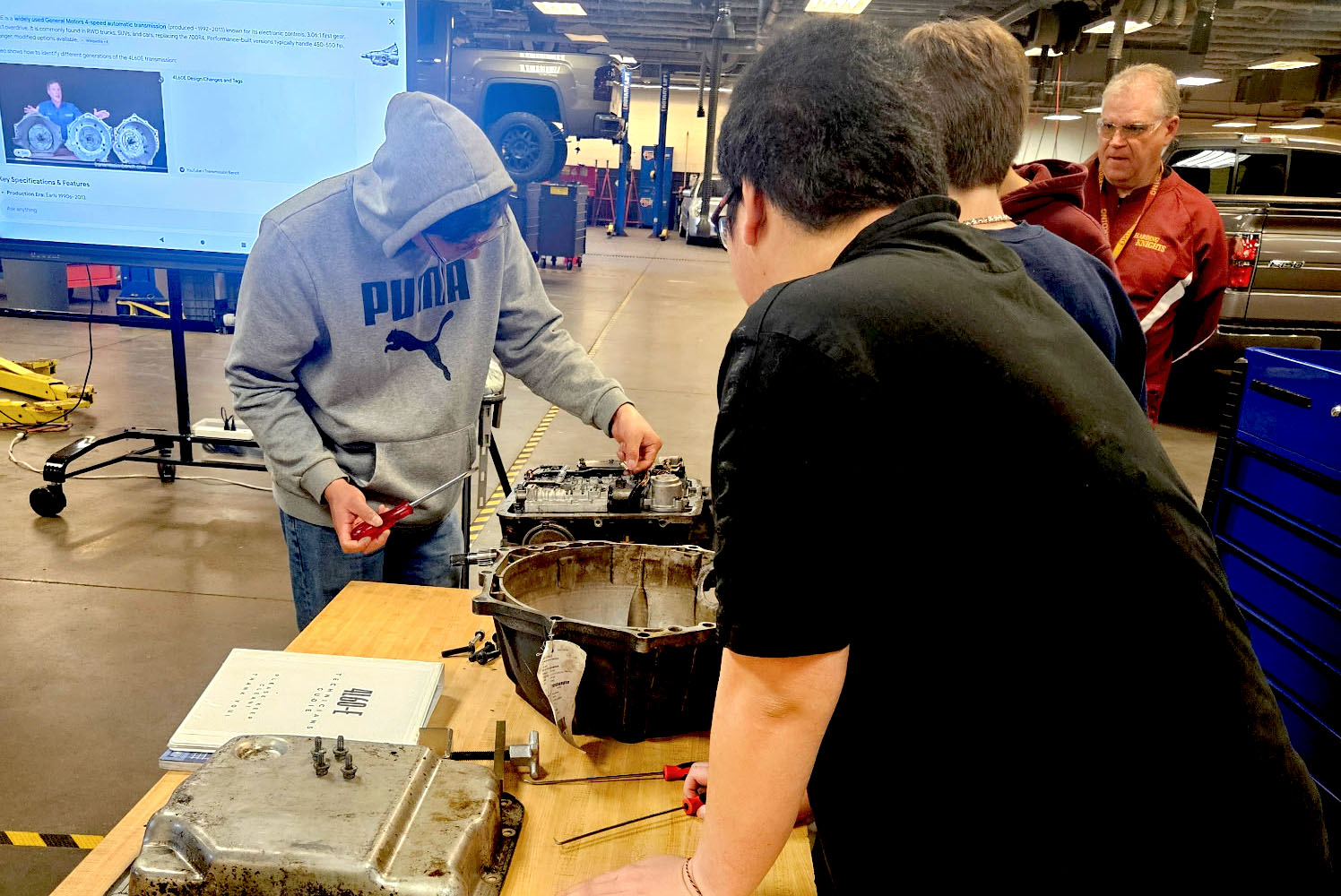 Three high school students around a table working on the transmission of a car.