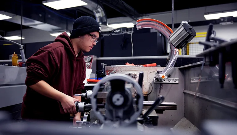 student in hoodie and beanie is gaining practical skills on a grinder