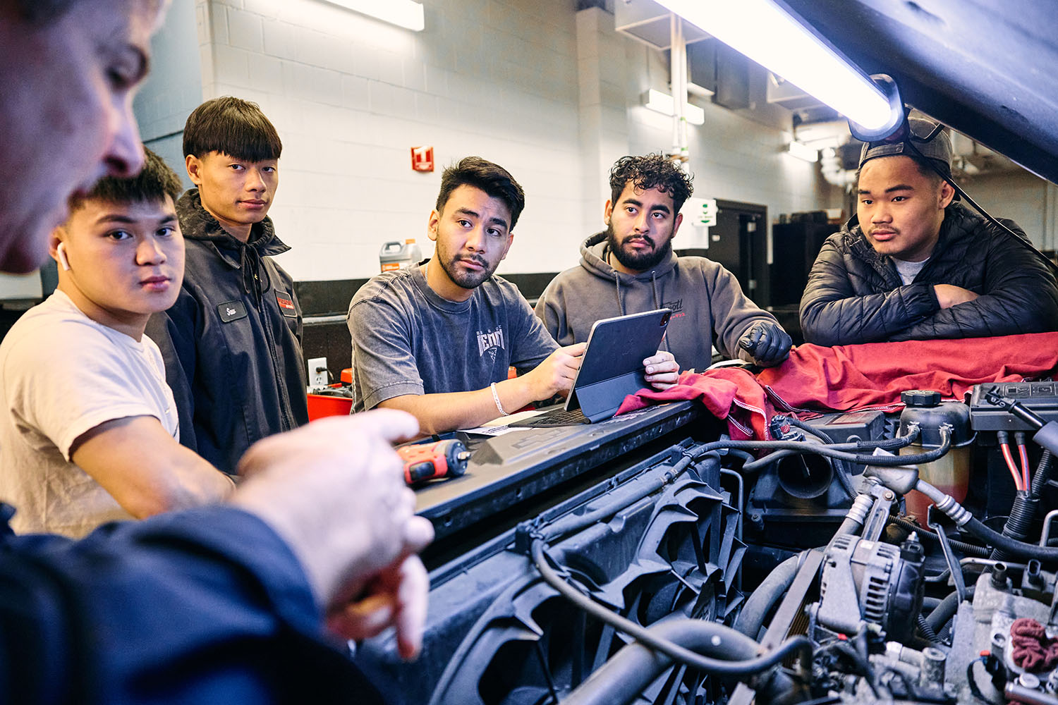 instructor demonstrating electrical diagnostics on vehicle component to students in automotive training lab