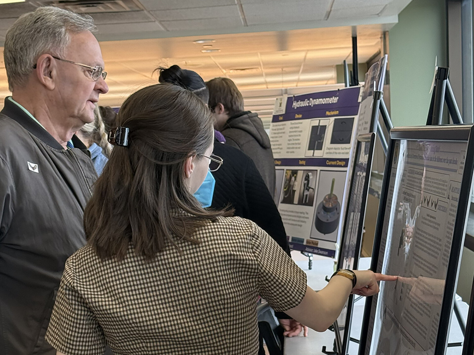 Dede Baltus at Research Showcase explain her project to an older man demonstrating student success.