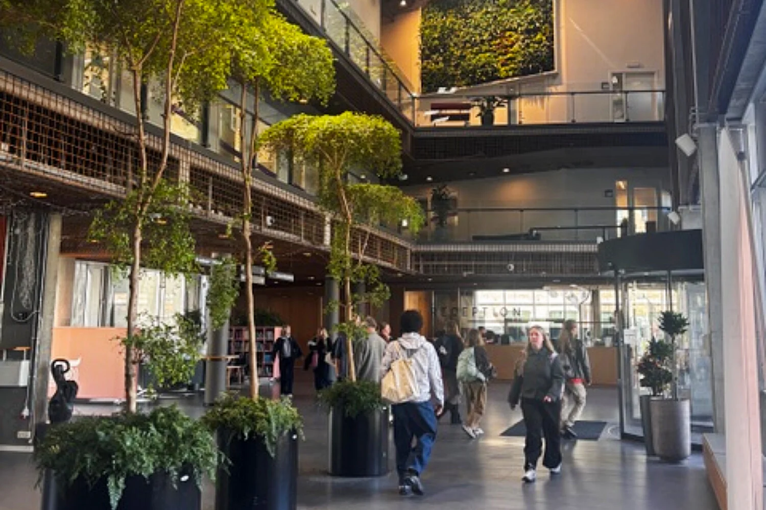 Modern university campus interior with students, indoor greenery, collaborative spaces, and sustainable architecture at Copenhagen higher education facility
