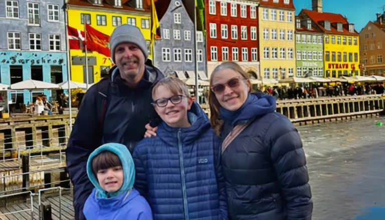 Family standing along Nyhavn waterfront in Copenhagen, Denmark with colorful historic buildings in the background, showcasing international travel and cultural exchange experience.