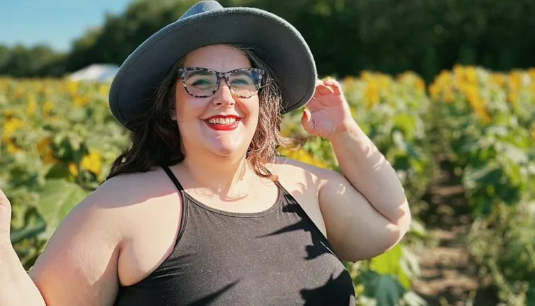 Saint Paul College Parenting program student standing in a sunflower field on a sunny day wearing a gray hat and glasses.