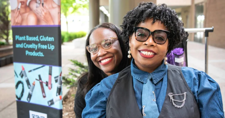 Tameka Jones and another woman at the Friends on the Lawn event showing off their lipstick brand Lip Esteem.