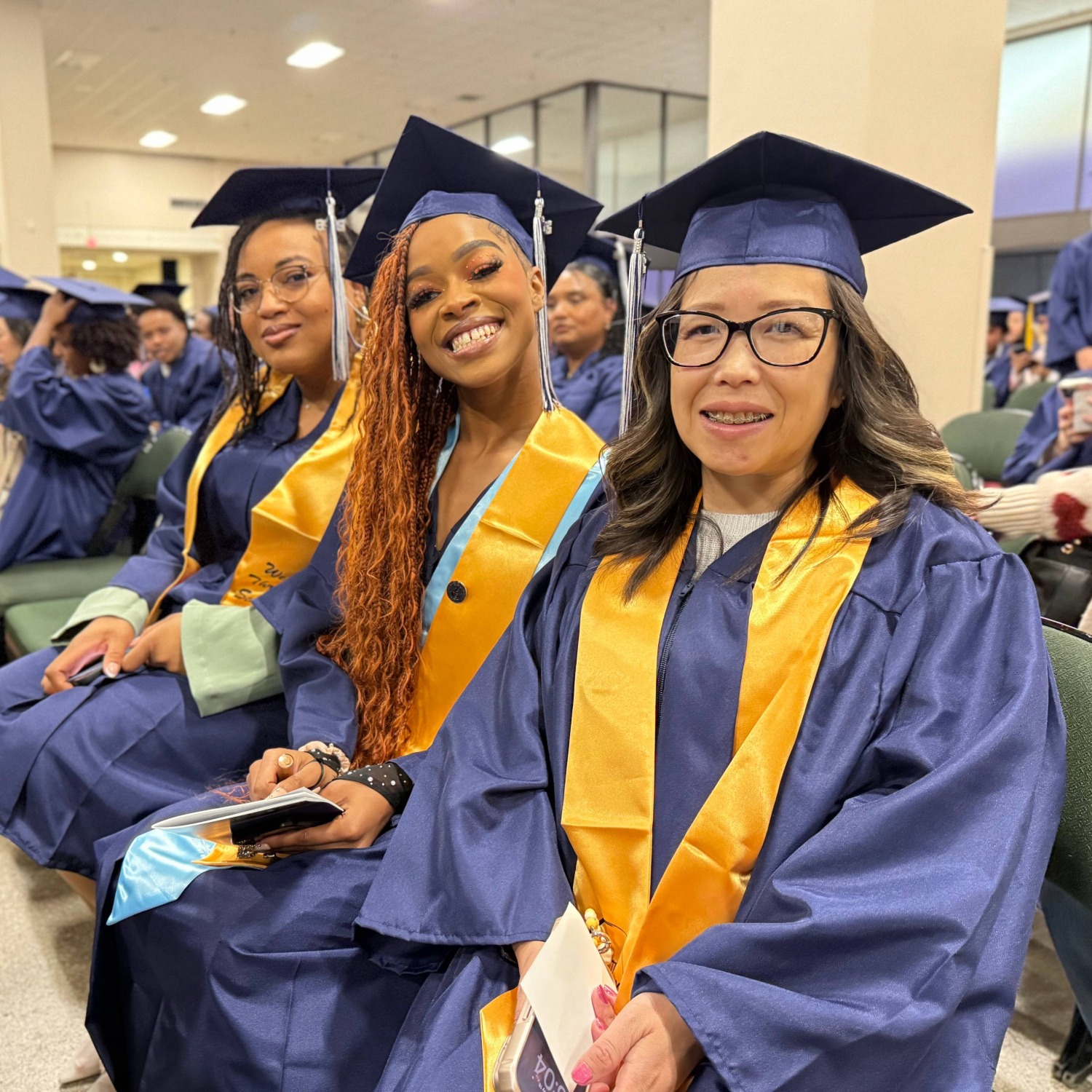 We Thrive students in cap and gown sitting in the graduate area at the Saint Paul College 2025-2026 graduation.