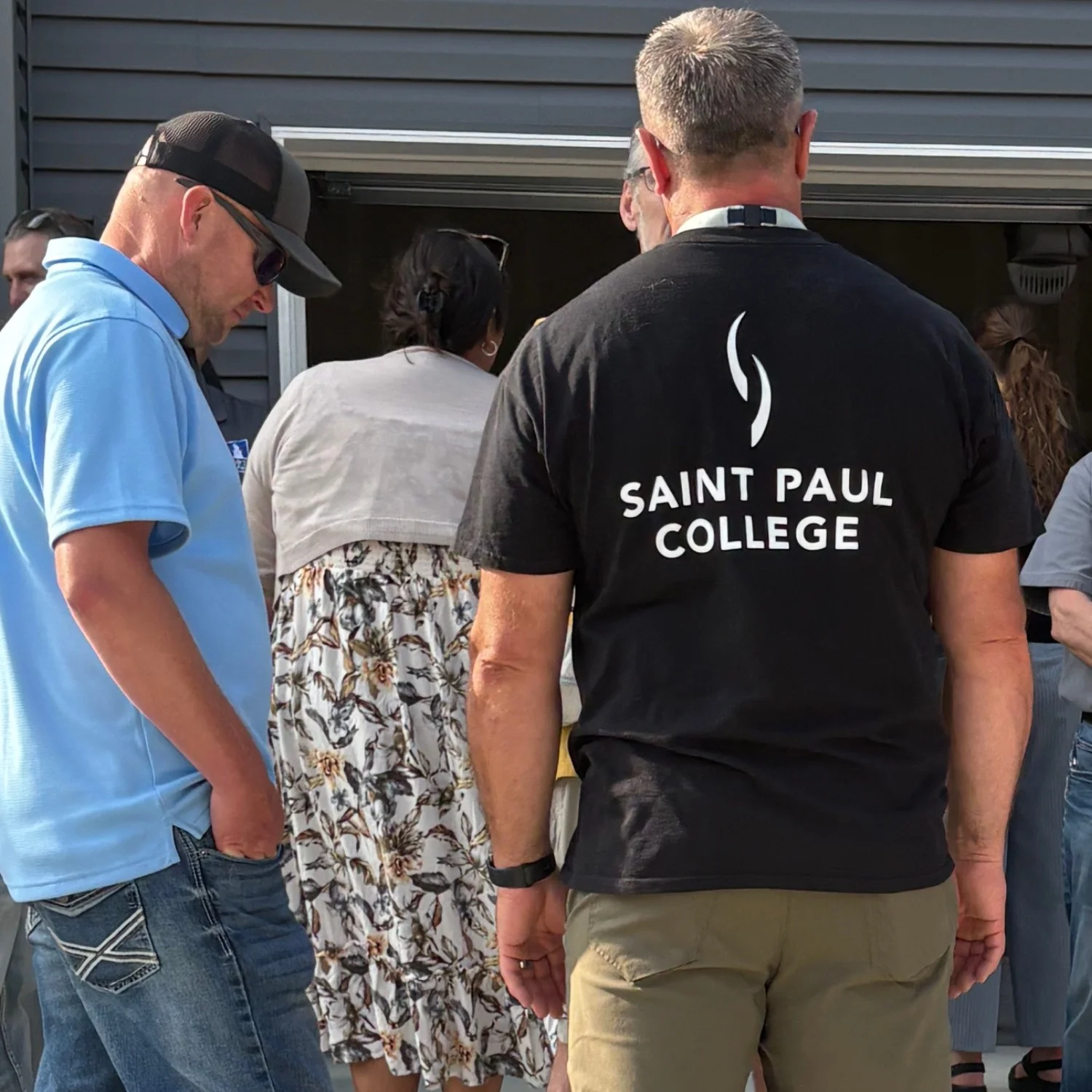 Thomas Leiskau wearing a Saint Paul College shirt while talking with others at the open house
