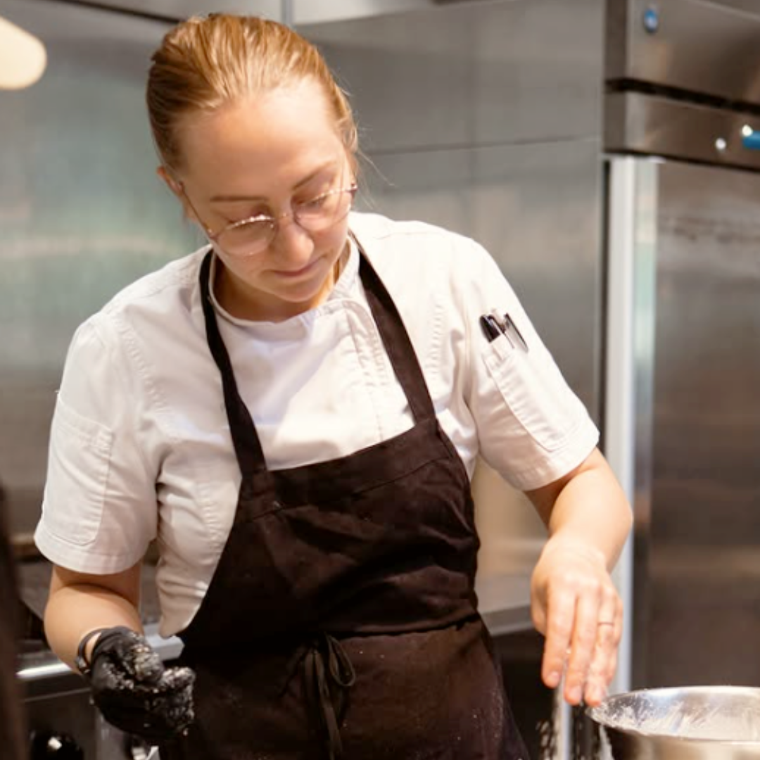 Beth Wills sprinkling an ingredient over a bowl she is working with in a kitchen